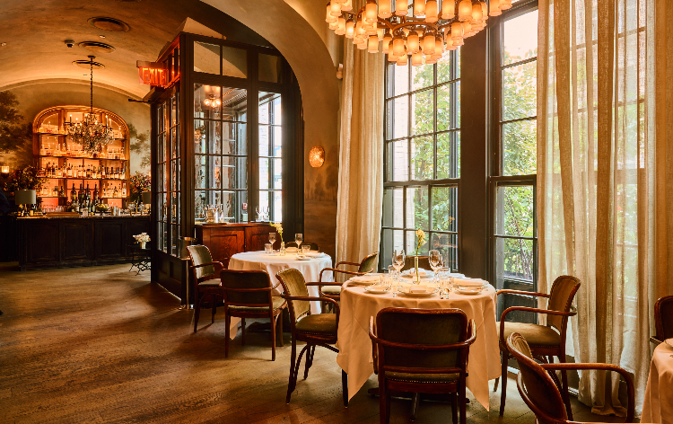 Vintage-style restaurant with warm lighting, arched ceiling, bar, and table set for two.