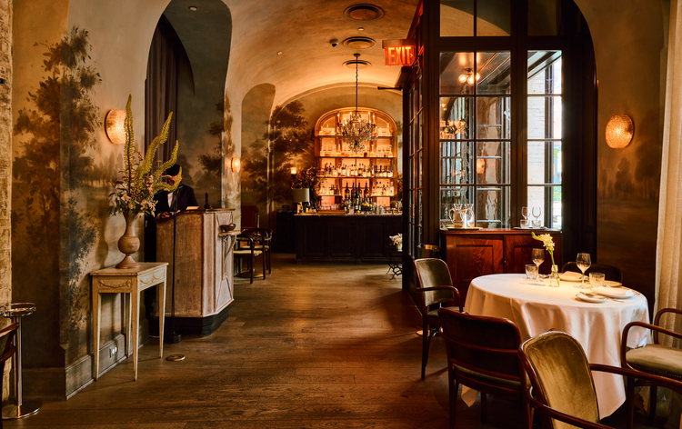 Vintage-style restaurant with warm lighting, arched ceiling, bar, and table set for two.